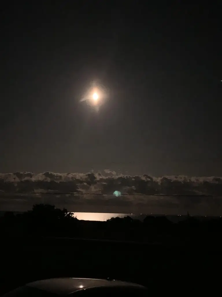Night sky with bright moon over ocean.